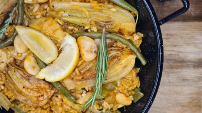 Delicious vegetarian paella featuring fennel, lemons, and green beans on wooden table.