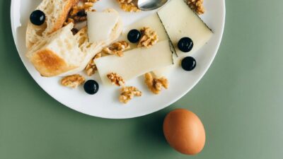 A stylish breakfast plate featuring cheese, walnuts, olives, and bread on a green background.