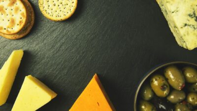 A delectable cheese platter featuring various cheeses, crackers, and olives on a slate background.