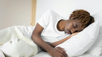 A serene image of a man sleeping peacefully on a white pillow and blanket indoors.