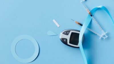 Flat lay of a diabetes monitoring kit with syringes and glucose meter on a blue background.