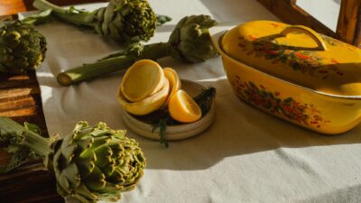 Rustic kitchen scene featuring artichokes, lemons, and a vintage yellow dish in warm sunlight.