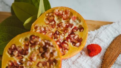 Top view of a sliced pomegranate with a raspberry on a cutting board, depicting freshness.