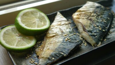 Delicious grilled mackerel served on a plate with lime slices and sprinkled sesame seeds.