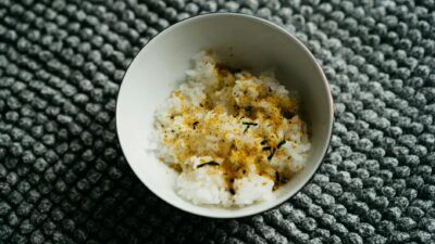 Close-up of Japanese rice bowl topped with furikake, a traditional seasoning, on a textured surface.