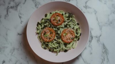 Colorful vegan meal featuring zucchini noodles, tomato slices, and seeds on a marble top.