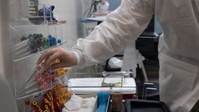 Person in lab coat selecting supplies from rack.