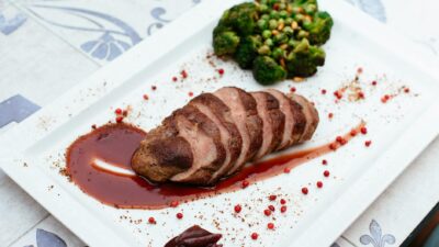 Deliciously plated duck breast with broccoli and sauce on a white plate.