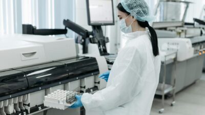 Laboratory worker in protective gear handling diagnostics equipment.