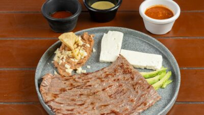 Delicious grilled skirt steak served with Mexican-style side dishes including cheese, refried beans, and sauces.