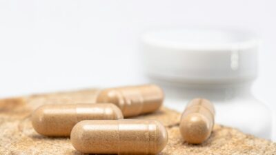 A close-up shot of brown capsules placed on a wooden surface with a blurred bottle in the background.