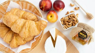 Flat lay of a French breakfast featuring croissants, camembert cheese, honey, and fresh fruits for a perfect start.