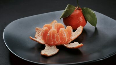 Close-up of a juicy peeled tangerine with leaves on a modern black plate.