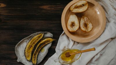 A rustic breakfast setup featuring baked pears, banana slices, and honey on a wooden table.