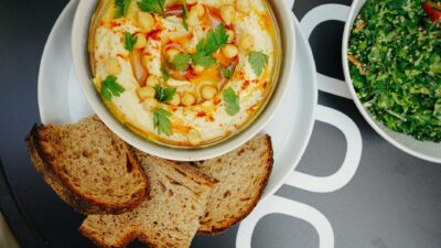 Top-view of homemade hummus garnished with parsley and served with bread slices, showcasing Mediterranean flavors.