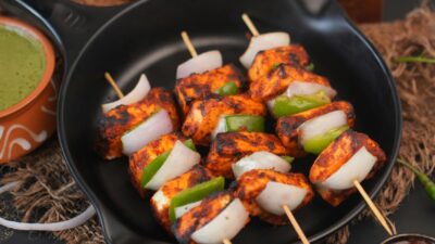 Close-up of grilled paneer skewers with bell peppers and onions on black plate.