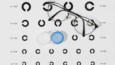 Close-up image of eyeglasses and contact lens case on a Snellen eye chart for vision testing.