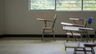 Quiet empty classroom interior with school desks by a large window.
