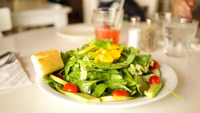 Healthy green salad with cherry tomatoes, lettuce, and mango on a white plate with bread.