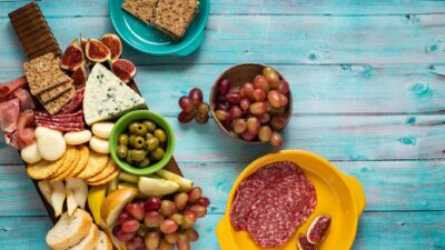 A vibrant display of cheeses, cold cuts, fruits, and crackers on a rustic wooden board.