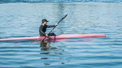 A person kayaking on calm waters in a vibrant pink kayak under clear skies.